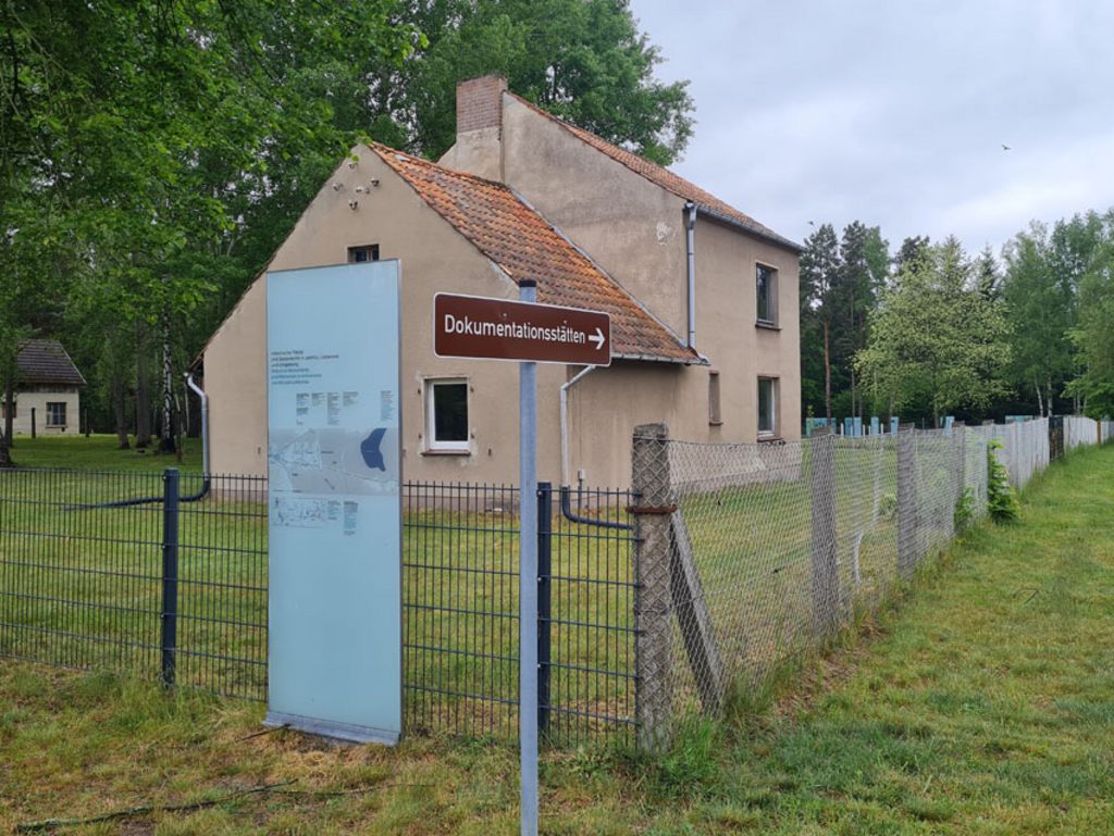 Foto: SBG/Seferens Das Bild zeigt das kleine Siedlungshaus, das für die Ntzung durch die Gedenkstätte saniert werden soll. Im Vordergrund stehen eine Informationstafel und ein Hinweisschild mit der Aufschrift "Dokumentationsstätten".