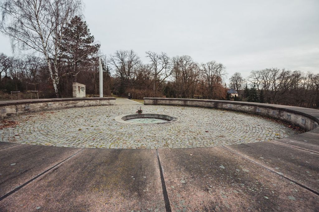 Im Vordergrund blickt man in das von einer kniehohen Mauer eingefasste sogenannte Ringgrab; im Hintergrund links befindet sich die Gedenkwand.